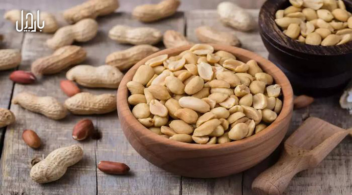 یک کاسه بادام زمینی و مقدار بادام زمینی با پوست در اطراف آن