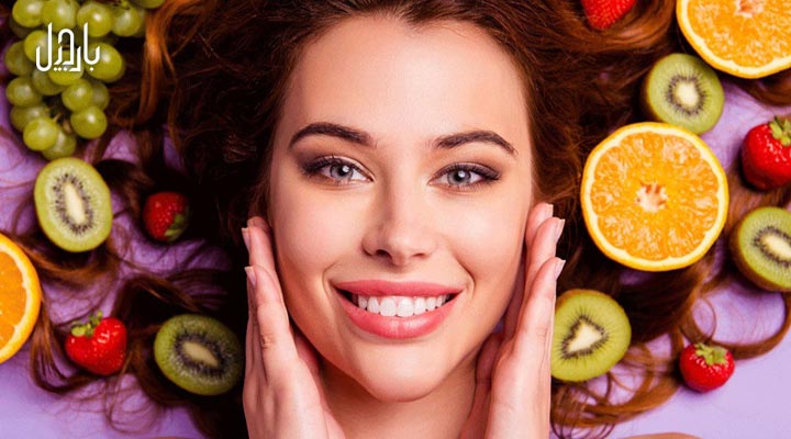 خانمی در حال نشان دادن پوست صورت خود و مقدار زیادی میوه مفید برای پوست