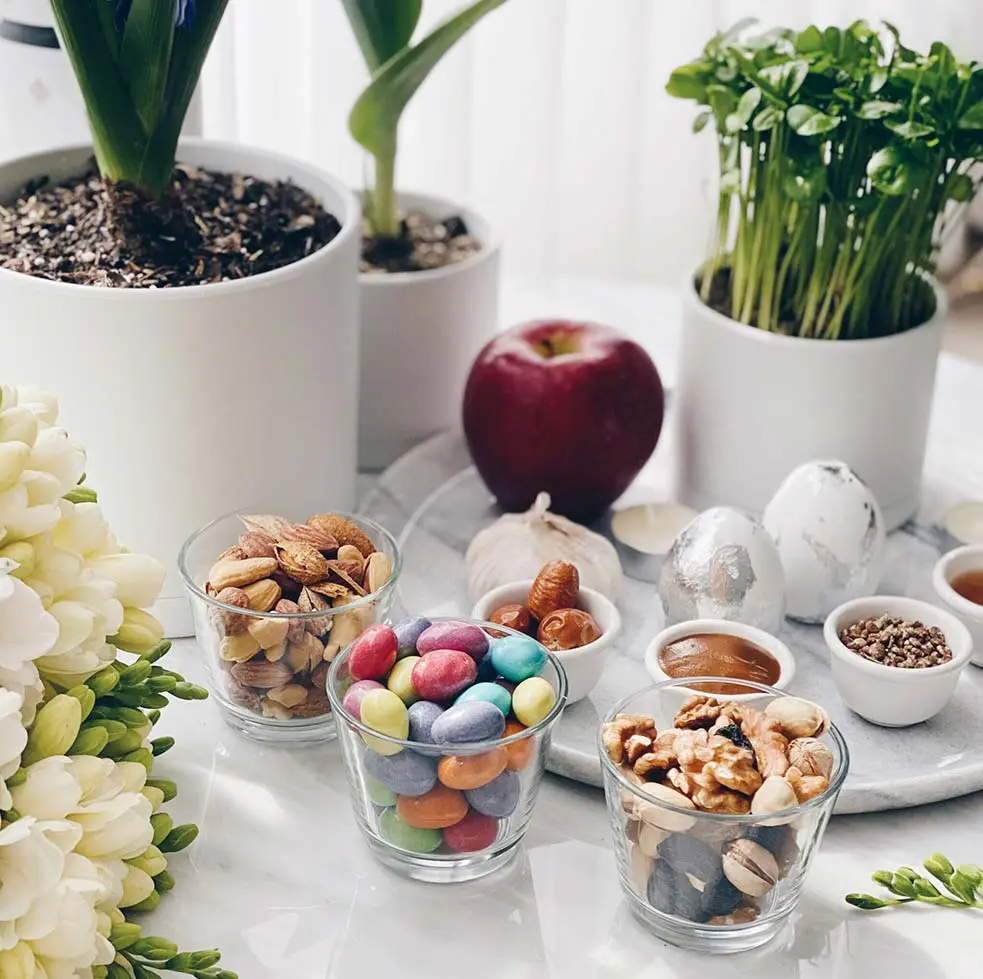 کاسه های آجیل عید روی میز در کنار چند گلدان