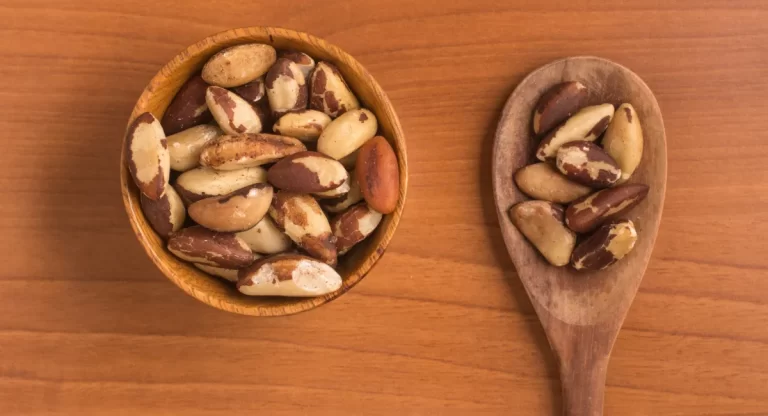 یک کاسه پر بادام برزیلی و یک قاشق چوبی پر بادام برزیلی روی سطح صاف