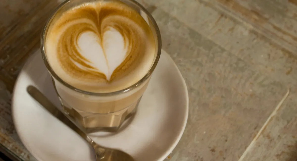 یک فنجان قهوه لاته با تزئین قلب به همراه یک قاشق چای خوری