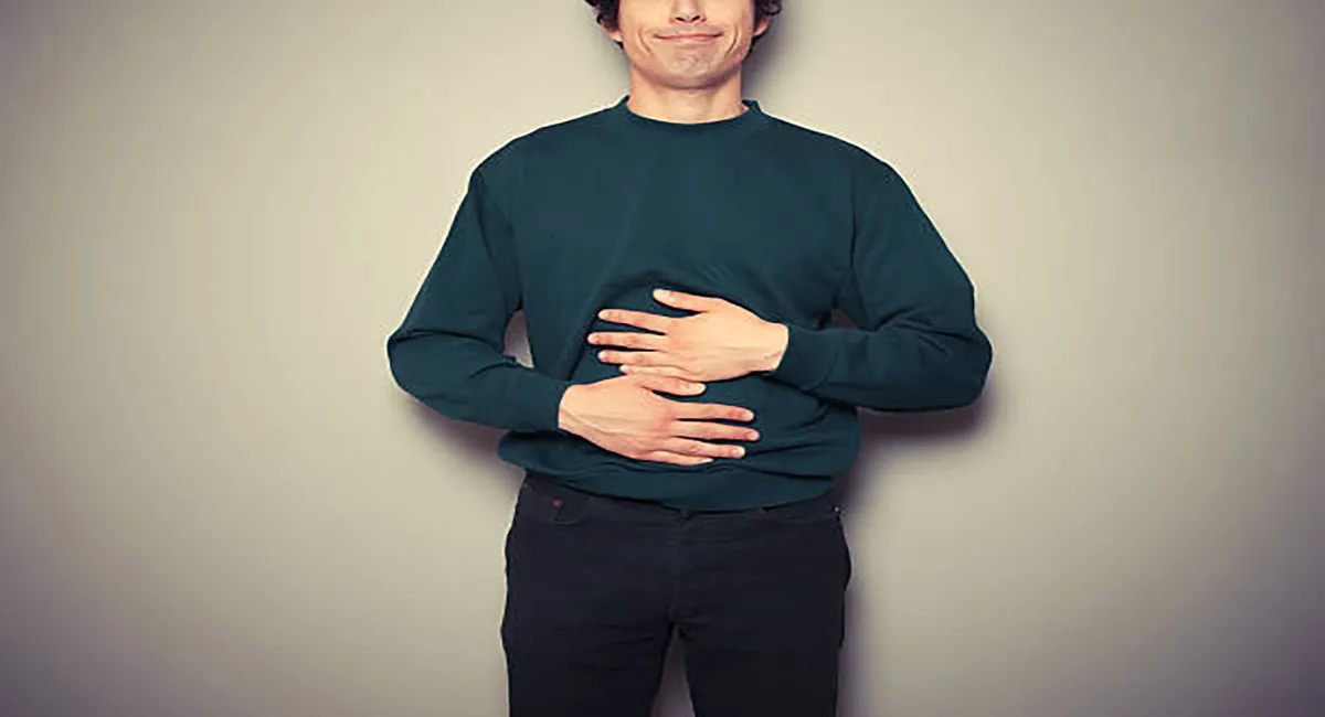 یک مرد تکیه داده به دیوار در حال فشردن شکم خود به دلیل دل ضعفه