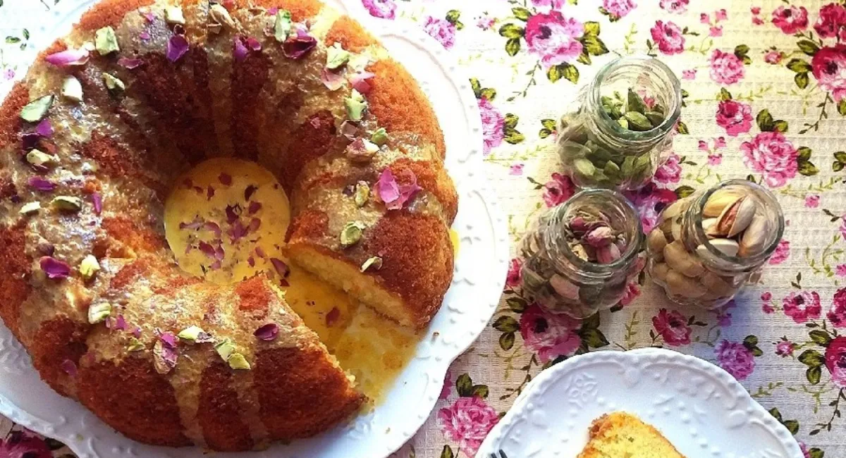 یک کیک گلاب و پسته با لعاب و تزئینات و چن ظرف کوچک پسته و گل محمدی