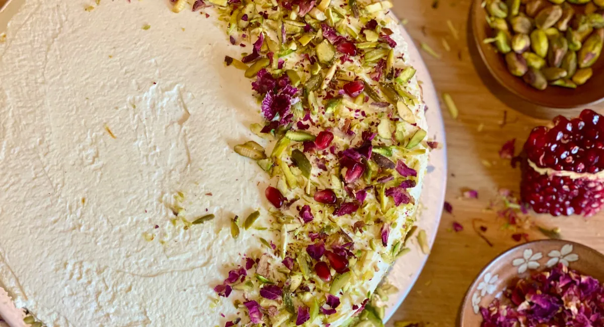 یک کیک گلاب و پسته تزئین شده به همراه مقداری گل رز و یک کاسه پسته خرد شده و کمی دانه انار