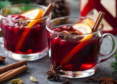 دو لیوان نوشیدنی قرمز زمستانی با تزئین لیمو و دارچین