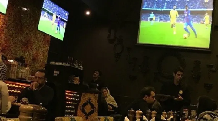 افرادی نشسته در کافه در حال تماشای فوتبال