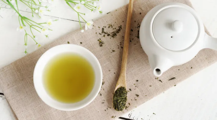 یک فنجان چای سبز، یک قوری، یک قاشق چوپی پر از چای سبز آسیاب شده