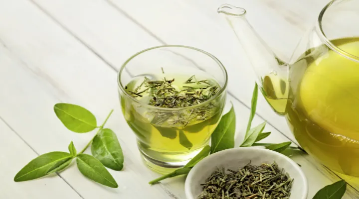 یک فنجان چای سبز و مقداری برگ چای و یک کاسه چای خشک و قوری پر از چای سبز