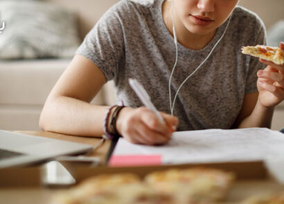 دانشجویی در حال درس خواندن با لپ تاپ و غذا خوردن